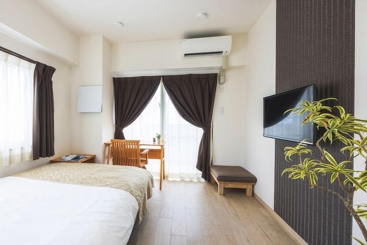 Una habitación de hotel con cama, escritorio, silla, televisor y planta.