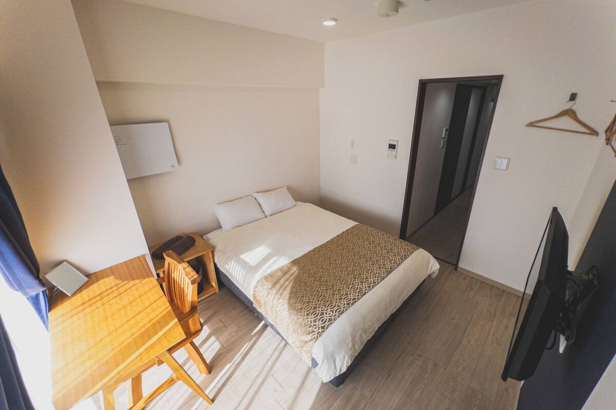 A hotel room with a bed, a desk, a chair, a TV, and a wardrobe.