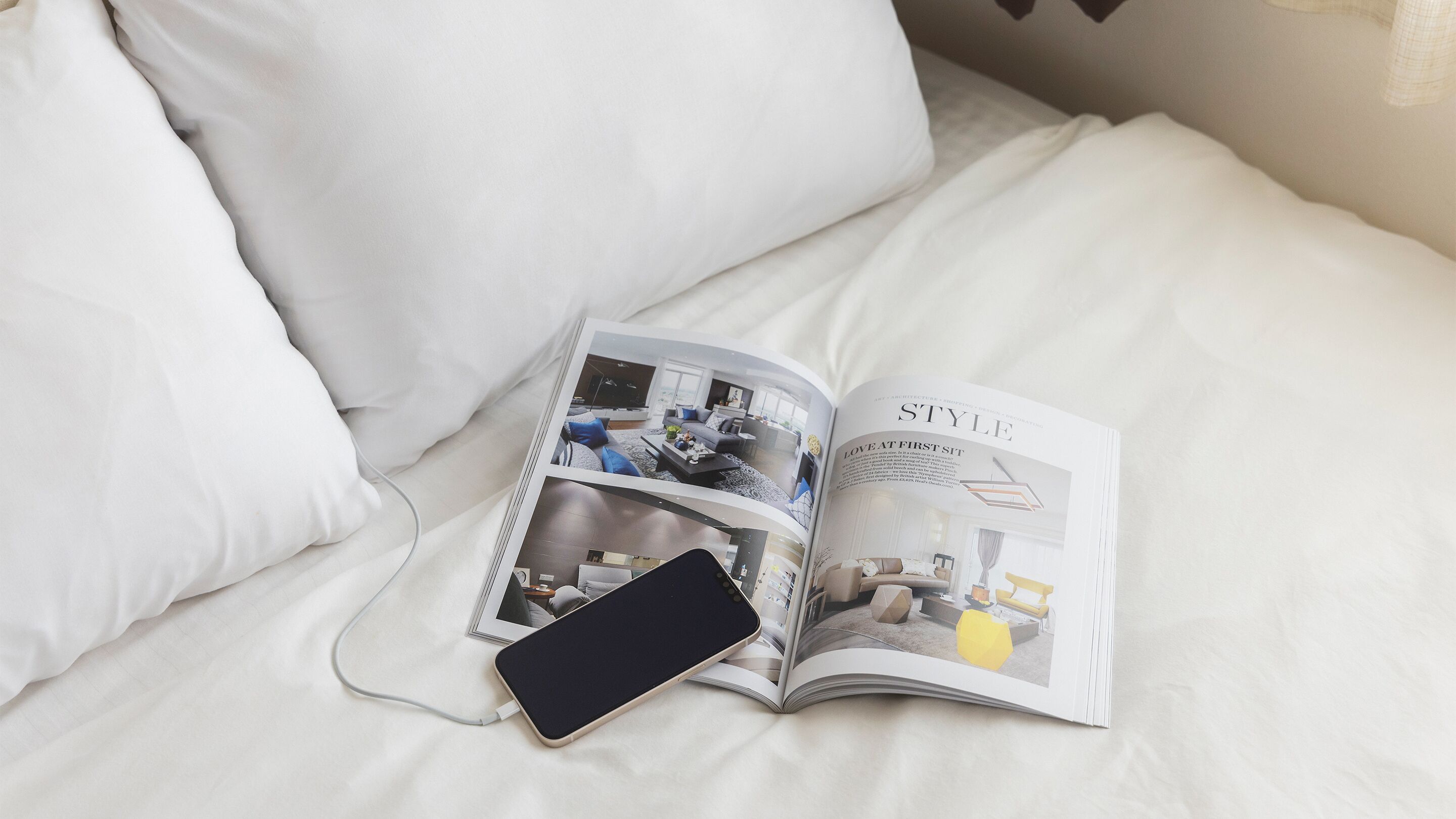 A magazine open on a bed with a smartphone charging, featuring a modern living room interior.