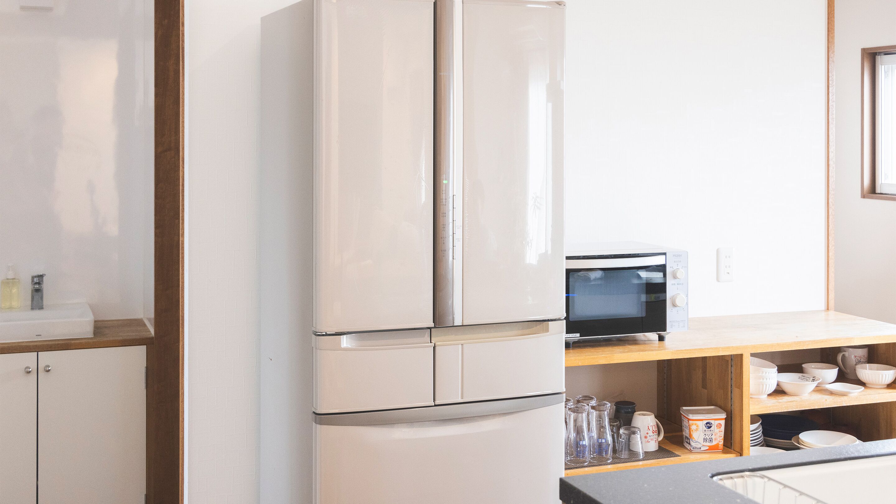 Een keuken met een witte koelkast, een magnetron en een houten plank met servies en glazen.