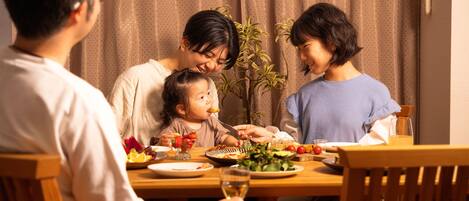 Une famille est assise autour d’une table en bois, et on peut voir différents plats, un verre de vin et une plante en pot à l’arrière-plan.