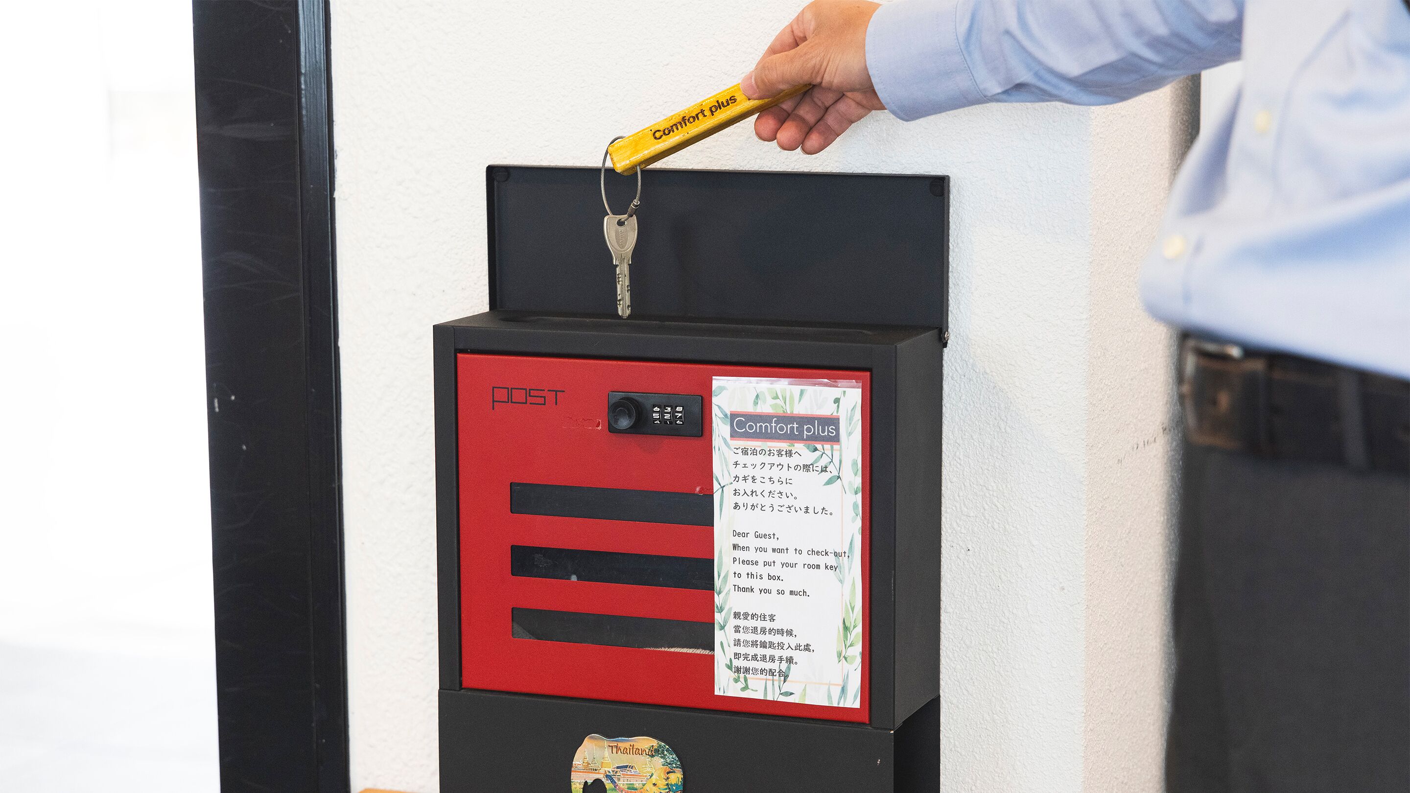 A red and black hotel mailbox with a key inserted, a sign with instructions, and a Thailand map sticker.
