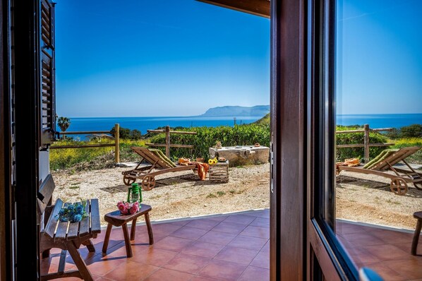 Relax in a serene outdoor space with ocean views and distant hills, featuring comfortable loungers and a small table.