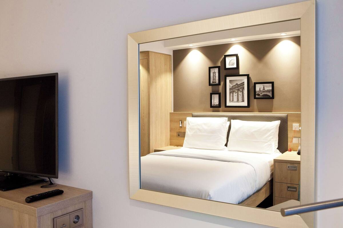 Una habitación de hotel con una cama, un televisor y un espejo que refleja la habitación.