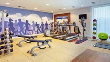 A gym with treadmills, a bench, dumbbells, and a wall mural of runners.