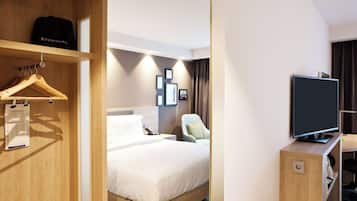 Habitación de hotel con cama de madera, televisor sobre un mueble, una silla y un escritorio con computadora.
