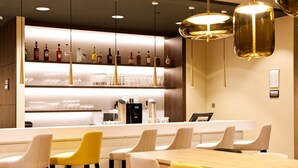Una zona de bar con una barra larga, varios taburetes y una variedad de botellas y vasos en estanterías.
