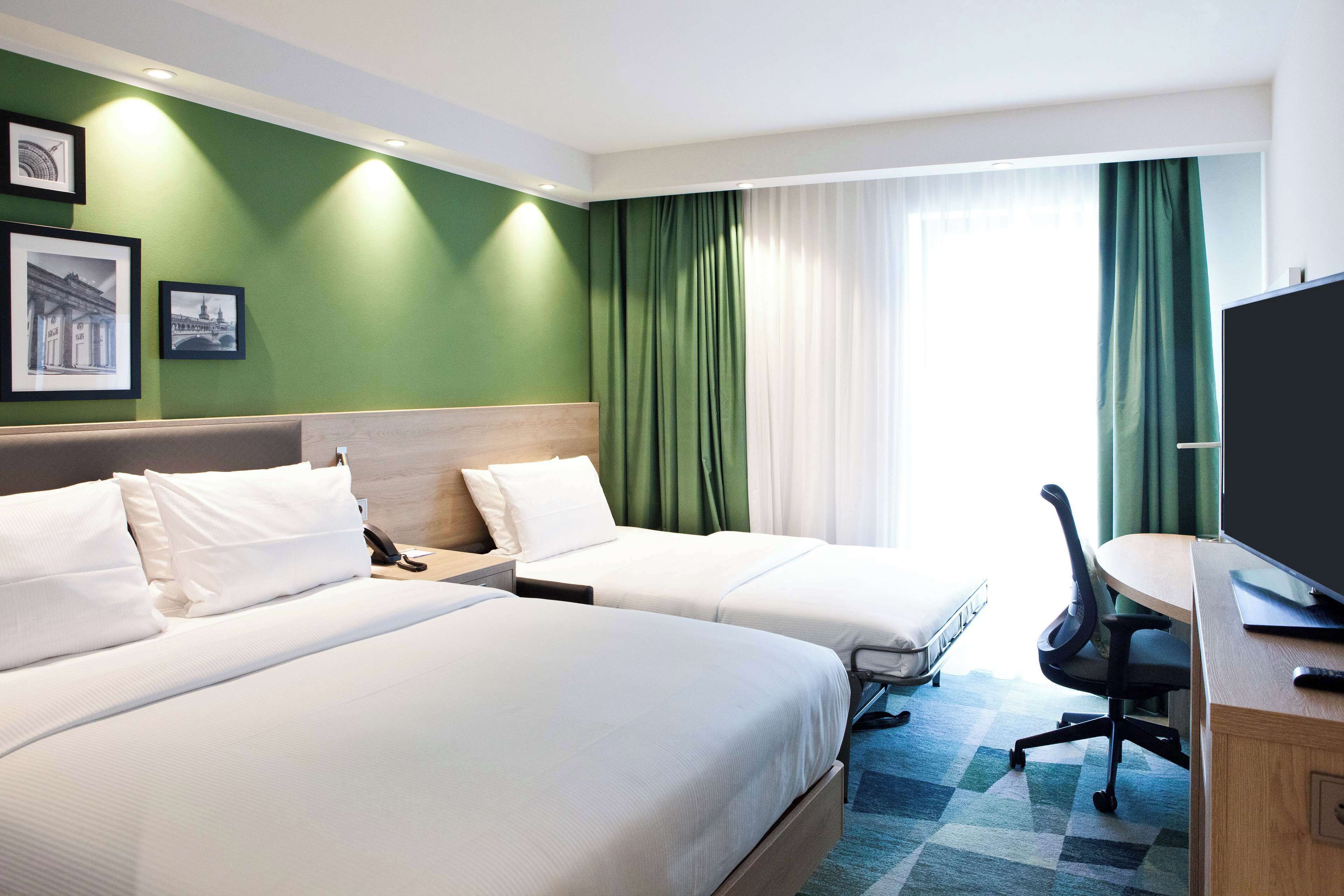 Une chambre d’hôtel avec deux lits, un bureau avec une chaise, une télévision et une fenêtre avec des rideaux.