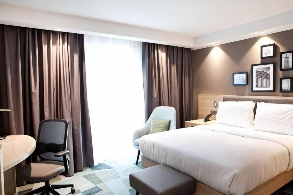 Una habitación de hotel con cama, escritorio, silla, mesita de noche y cortinas.
