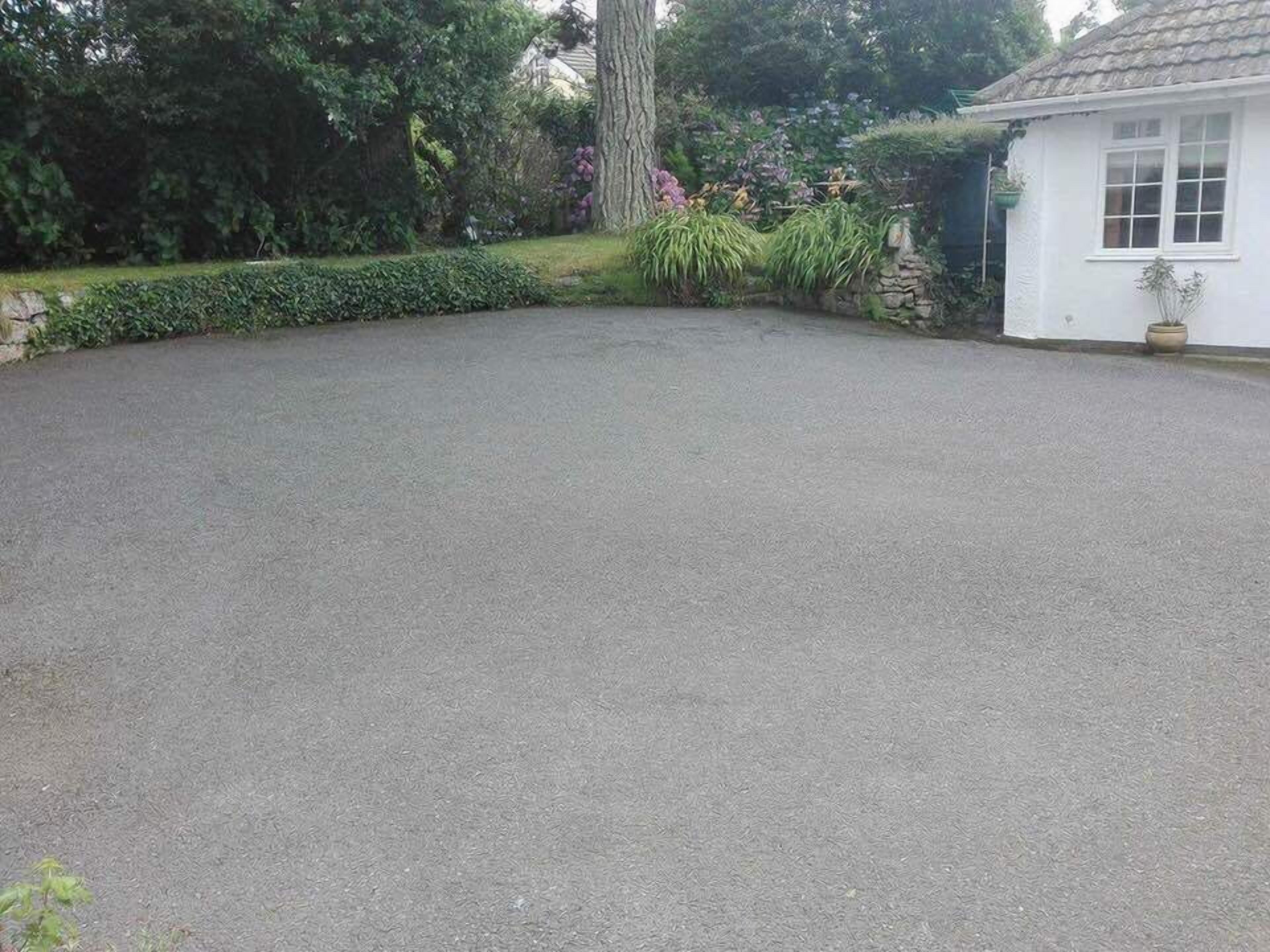 A paved driveway leading to a white building with a stone wall and a potted plant.