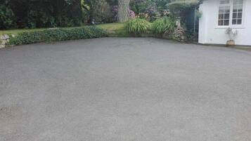 A paved driveway leading to a white building with a stone wall and a potted plant.