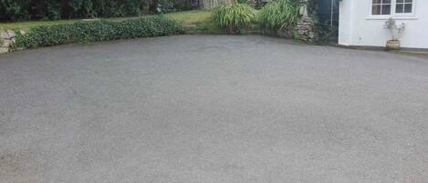 A paved driveway leading to a white building with a stone wall and a potted plant.