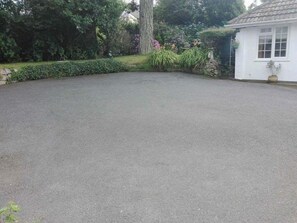Un camino pavimentado que conduce a un edificio blanco con un muro de piedra y una maceta.