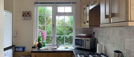 A kitchen with wooden cabinets, a gas stove, a microwave, and a window with a view of greenery.