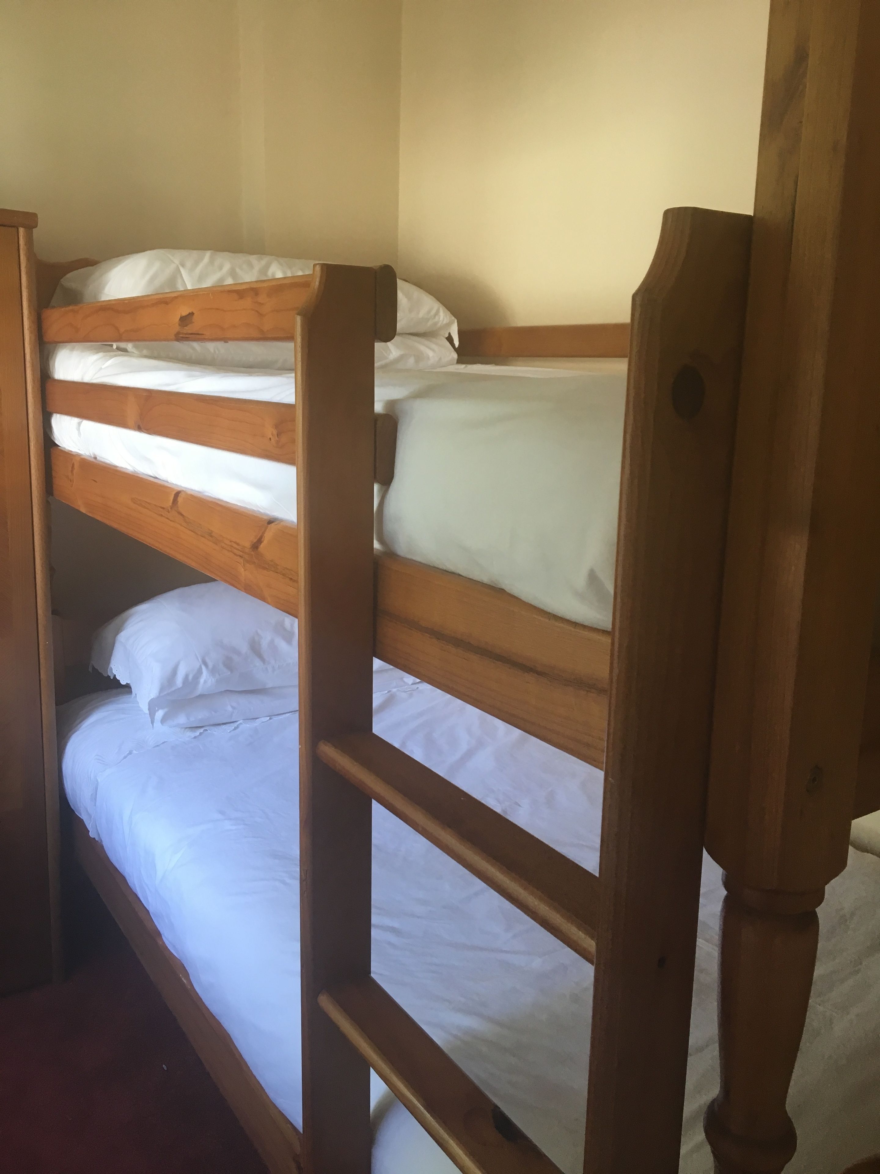 A bunk bed with wooden frames and white bedding.