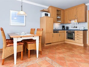A kitchen with wooden cabinets, a dining table with chairs, and a tiled floor.