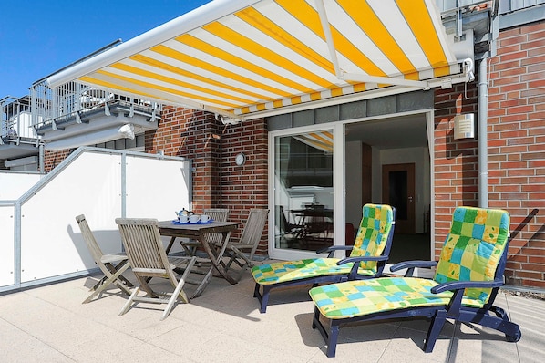 Une terrasse avec deux chaises en bois, une table et un auvent à rayures jaunes.