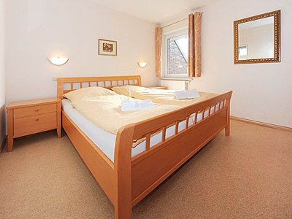 Quarto com cama de madeira, mesa de cabeceira, janela com cortinas e espelho fixado na parede.