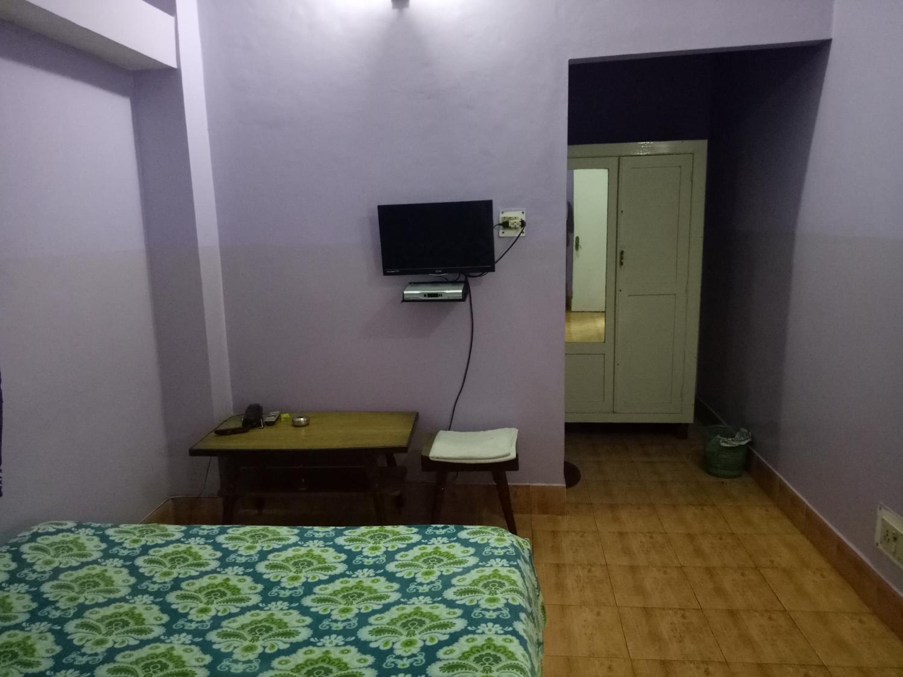 A small, simple room with a bed, a desk, a chair, and a television.