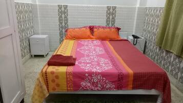A neatly made bed with a patterned bedspread, a bedside table, and a green rug.