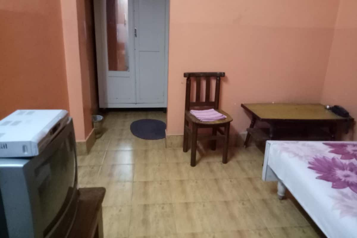 Una habitación pequeña con cama, una mesa, una silla, televisor y puerta.