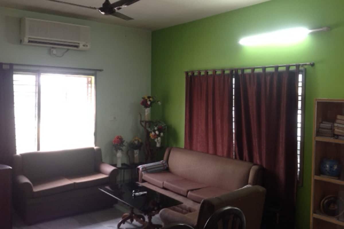Una sala de estar con un sofá, una mesa de centro, un ventilador de techo, un equipo de aire acondicionado, una ventana con cortinas y una estantería.