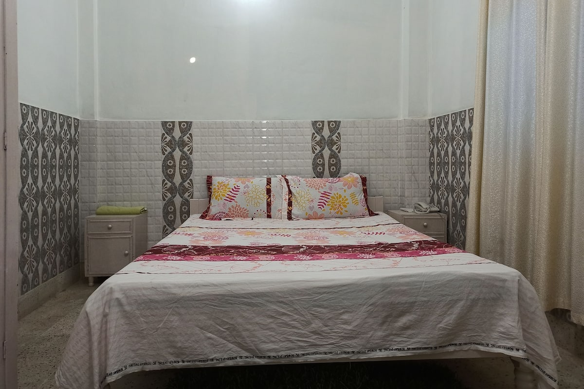 Un dormitorio con una cama, dos mesitas de noche y una lámpara de pared.