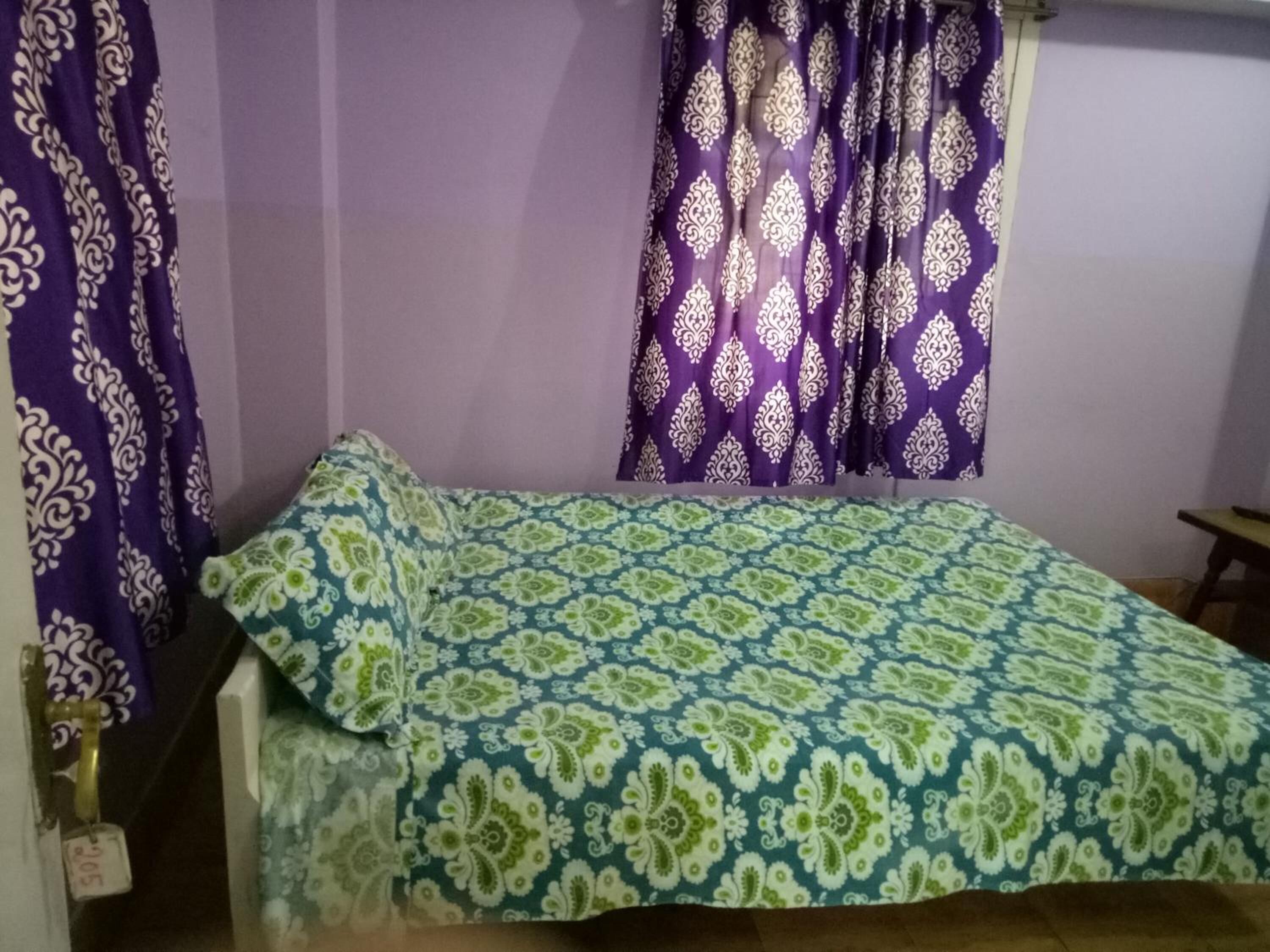 A room with a bed, purple curtains, and a patterned bedspread.