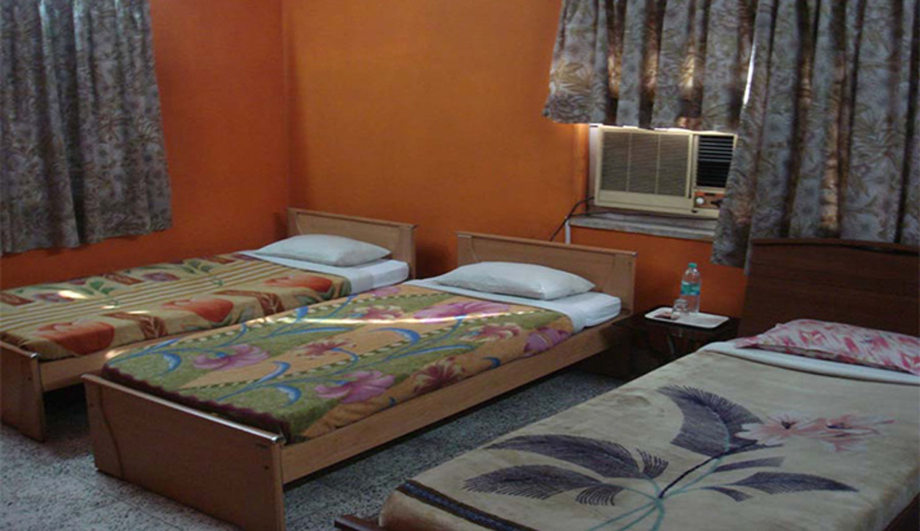 A room with two single beds, a small table with a bottle, and an air conditioning unit.