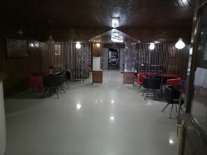 Een ruim, modern interieur met een hoge plafond en een open centrale ruimte. Er zijn verschillende zithoeken met stoelen en tafels, en een zichtbaar baliegedeelte.