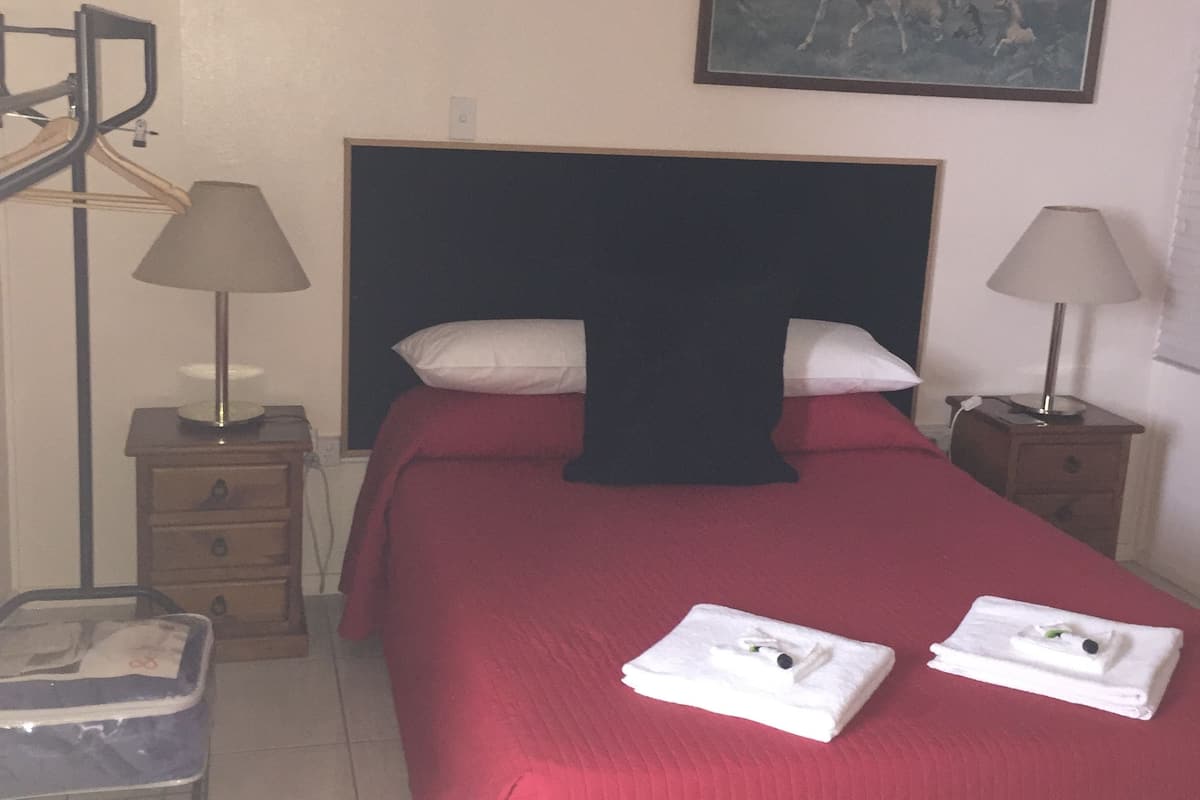A hotel room with a bed, a nightstand, a lamp, a wardrobe, and an air conditioning unit.