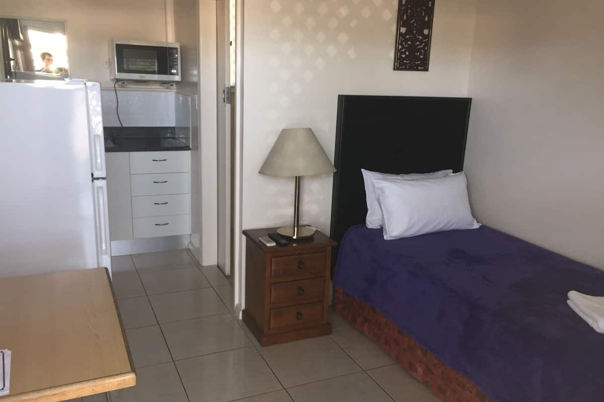 A bedroom with a bed, a nightstand, a lamp, a dresser, a microwave, and a small table.