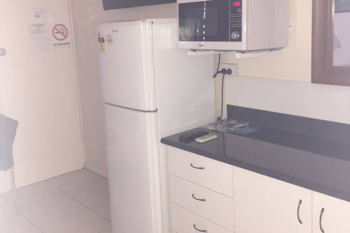A compact kitchen with a white refrigerator, a microwave, and a black TV mounted above it.