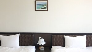 Een hotelkamer met twee bedden, een nachtkastje met een lamp, en een lijst met een foto van een strand aan de muur.