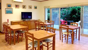 Een eetgedeelte met houten tafels en stoelen, een televisie en ingelijste foto’s aan de muur.