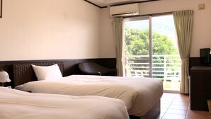 Een hotelkamer met twee bedden, een balkon met uitzicht op groen en een bureau met een lamp.