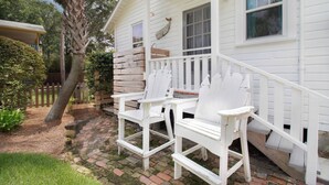 A white wooden house with a porch, white chairs, and a brick pathway.