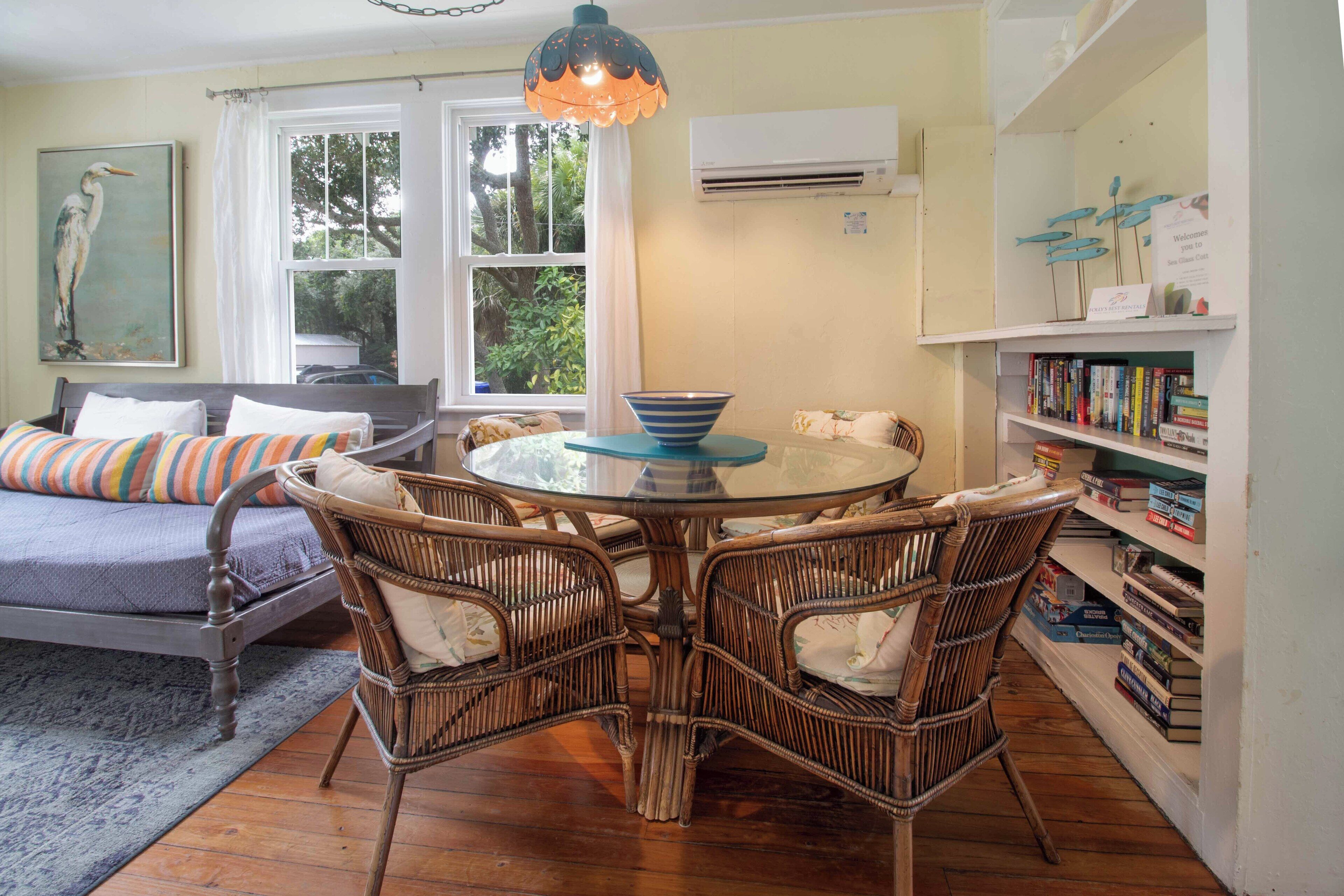 Un salon chaleureux avec un canapé, des fauteuils en osier, une table à plateau en verre et une bibliothèque remplie de livres.