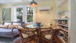 A cozy living room with a sofa, wicker chairs, a glass-top table, and a bookshelf filled with books.