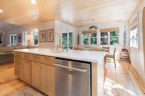 A modern kitchen with wooden cabinets, a stainless steel dishwasher, and a large island with a sink. - Serene and Completely Renovated!~ Heron House (Folly Beach)