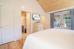 A bedroom with a large bed, a wardrobe, a television on the wall, and a sliding glass door leading to a balcony. - Serene and Completely Renovated!~ Heron House (Folly Beach)