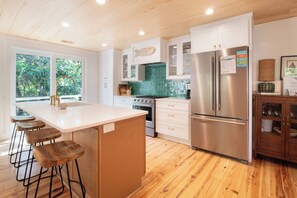 Cocina moderna con una isla central, taburetes de bar, un refrigerador de acero inoxidable y vistas a zonas verdes.