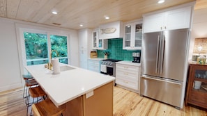 A modern kitchen with a central island, stainless steel appliances, and a view of greenery outside.