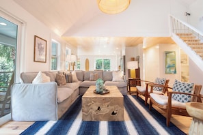 A spacious living area with a large sofa, a coffee table, and a staircase. - Serene and Completely Renovated!~ Heron House (Folly Beach)
