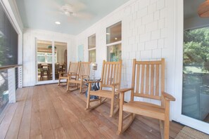 A covered patio area with wooden chairs and a glass table, white brick walls, and a view of the outdoors. - Serene and Completely Renovated!~ Heron House (Folly Beach)