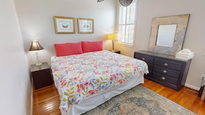 A bedroom with a floral bedspread, two red pillows, a dark dresser, a mirror, and two framed pictures on the wall.