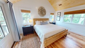 Un dormitorio con una cama grande, una mesita de noche, una obra de arte en la pared y una ventana con vistas a zonas verdes.