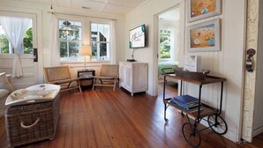 A cozy room with a wooden floor, wicker furniture, a ceiling fan, and a wall-mounted TV. - One house plus 2 cottages on the same lot~Family Houses (Folly Beach)