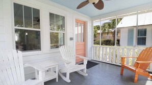 A covered porch with white and orange Adirondack chairs, a white rocking chair, and a wooden chair. - One house plus 2 cottages on the same lot~Family Houses (Folly Beach)