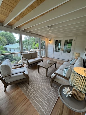 A sunlit room with a wooden ceiling, a sofa set, a coffee table, and a view of greenery outside.